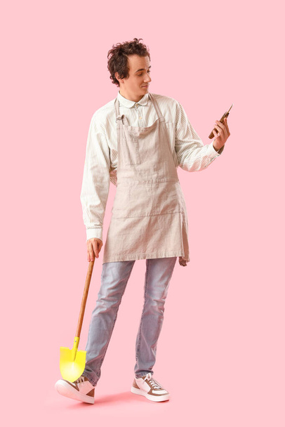 Jardinero masculino con tijeras de podar y pala sobre fondo rosa - Foto, Imagen