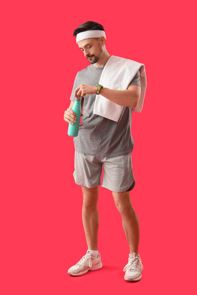 Sporty young man with bottle of water on red background - Photo, Image