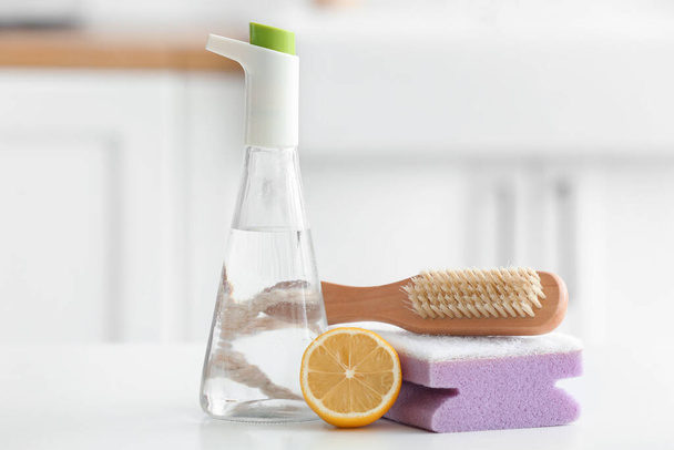 Bottle of vinegar, sponge, brush and lemon on table - Фото, изображение