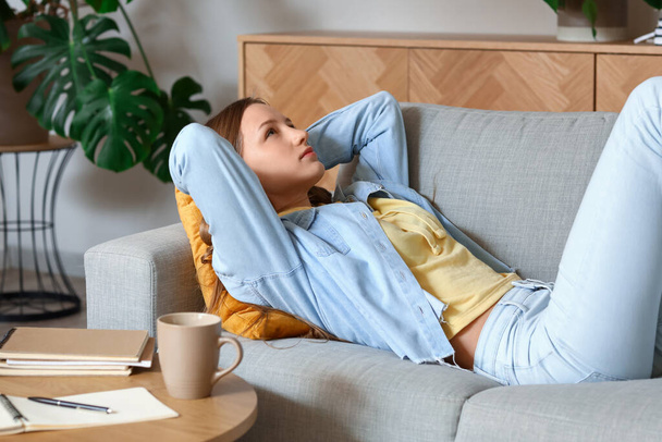Thoughtful teenage girl lying on sofa at home - Foto, Imagem