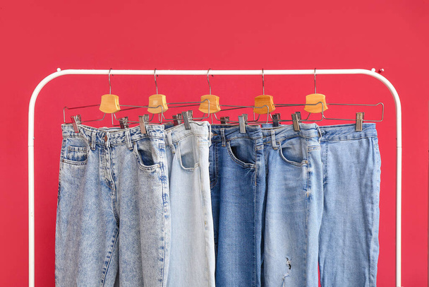 Rack with stylish jeans on red background, closeup - Φωτογραφία, εικόνα