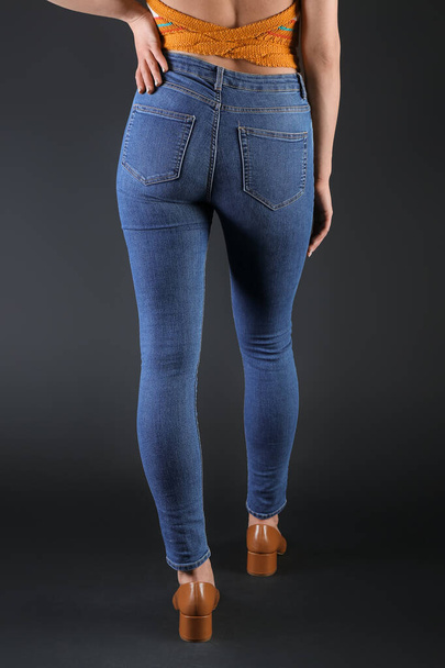 Young woman in skinny jeans on dark background, back view - Foto, imagen