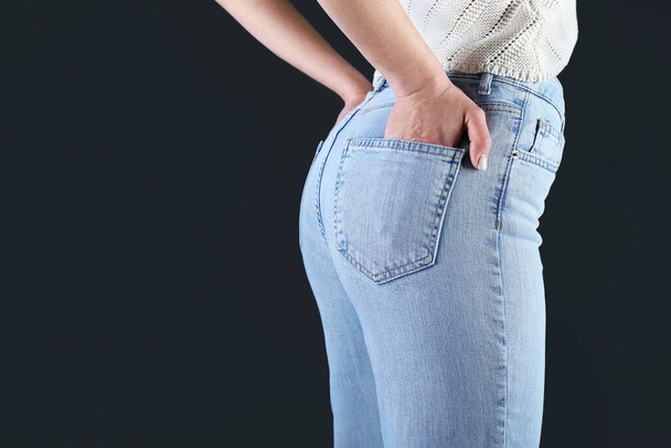 Молода жінка в стильних джинсах на темному тлі, крупним планом
 - Фото, зображення