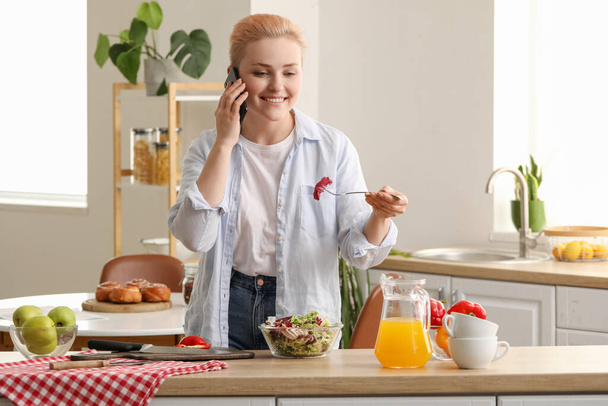 Fiatal nő zöldség saláta beszél mobiltelefon a konyhában - Fotó, kép