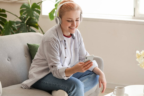 Young woman in headphones with mobile phone at home - Foto, afbeelding