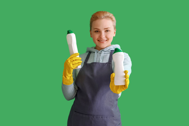 Young woman with bottles of detergent on green background - Foto, imagen
