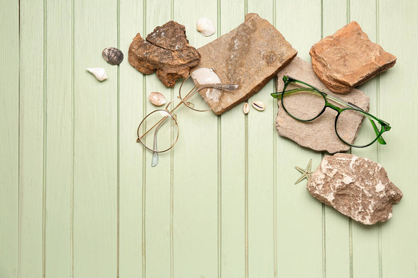Tyylikkäät silmälasit kivillä ja simpukoilla vihreällä puupohjalla - Valokuva, kuva
