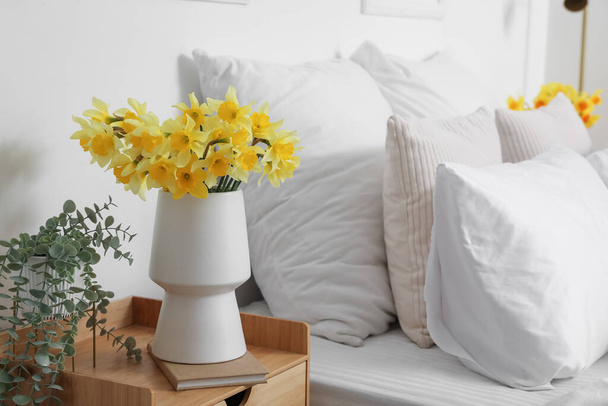 Váza s kvetoucími narcisy květiny a pokojová rostlina na nočním stolku - Fotografie, Obrázek