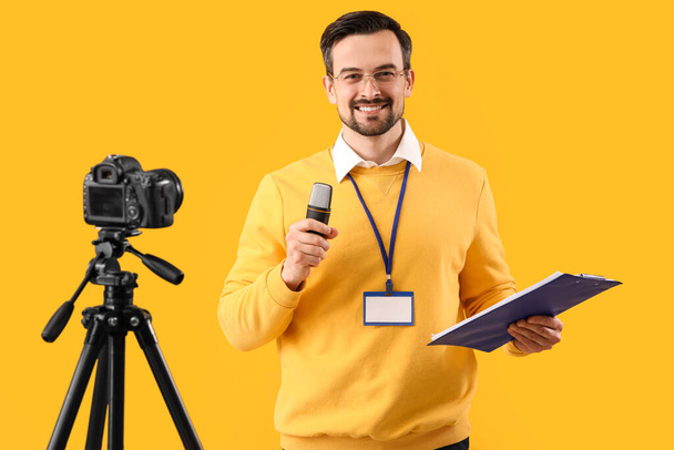 Férfi újságíró mikrofonnal és írótáblával videó sárga alapon - Fotó, kép