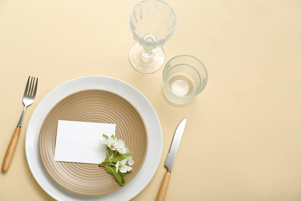Hermosa mesa con tarjeta de invitación en blanco y rama de árbol en flor sobre fondo beige - Foto, Imagen