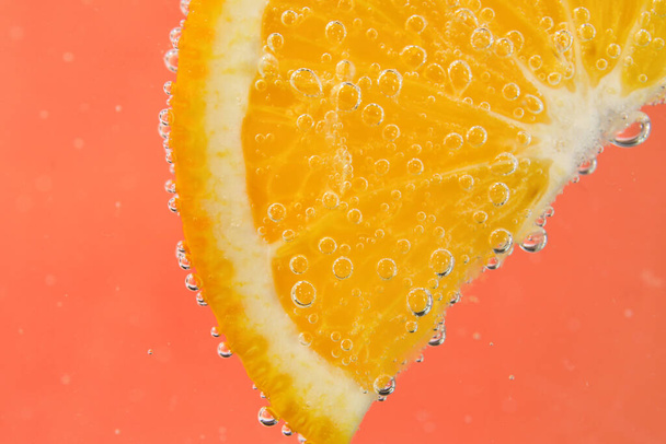 Orangenscheibe im Wasser mit Blasen auf rotem Hintergrund - Foto, Bild