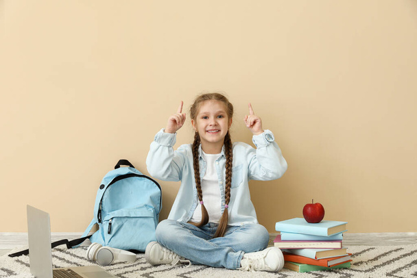 Petite fille avec des livres, pomme et sac à dos pointant vers quelque chose près du mur beige. Célébration Journée des enfants - Photo, image