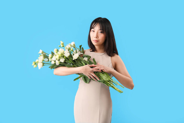 Güzel Asyalı kadın mavi arka planda bir buket Eustoma çiçeği tutuyor. - Fotoğraf, Görsel