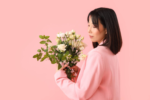 Mooie Aziatische vrouw met boeket van eustoma bloemen op roze achtergrond - Foto, afbeelding