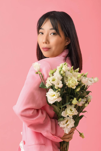 Beautiful Asian woman holding bouquet of eustoma flowers on pink background - Photo, Image