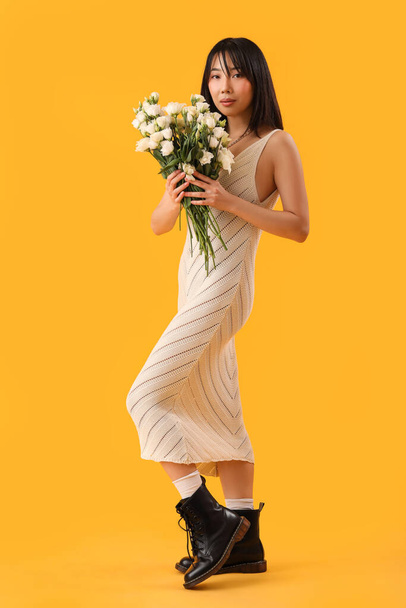 Beautiful Asian woman holding bouquet of eustoma flowers on yellow background - Фото, зображення