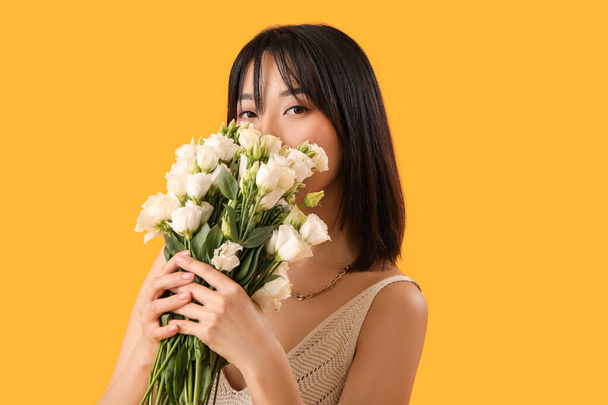 Bella donna asiatica che tiene bouquet di fiori di eustoma su sfondo giallo - Foto, immagini