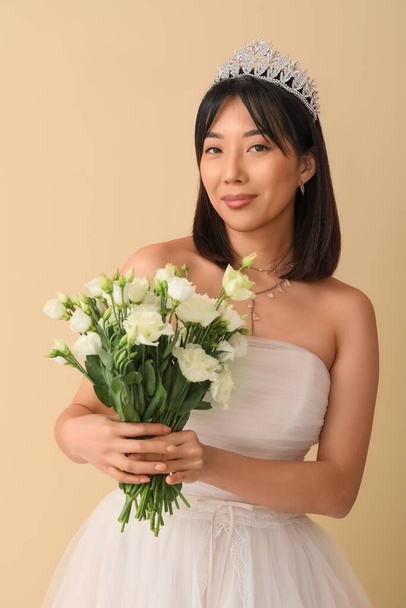 Hermosa novia asiática joven con ramo de flores de eustoma sobre fondo beige - Foto, Imagen
