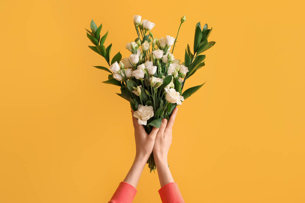 Sarı arka planda güzel bir buket Eustoma çiçeği olan bir kadının elleri. - Fotoğraf, Görsel