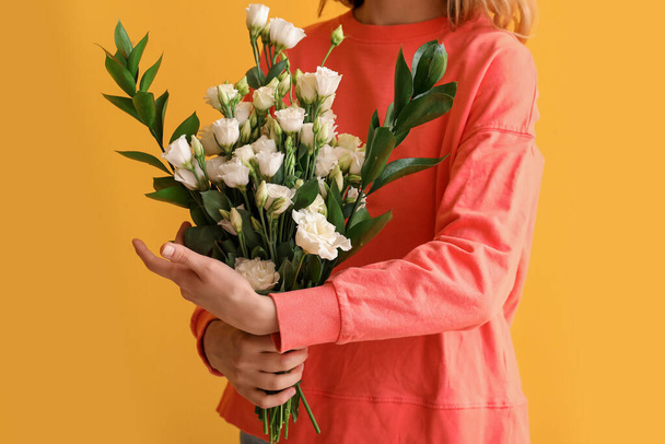 黄色の背景に美しい花の花束を持つ若い女性 - 写真・画像