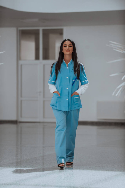 Una enfermera de uniforme azul parada en el pasillo de un hospital moderno.  - Foto, Imagen