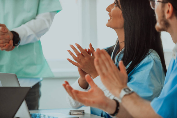  Un equipo de médicos y una enfermera aplaudiendo a su colega después de una presentación en una sala de reuniones.  - Foto, imagen