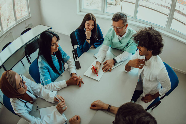 Top view of a group of multiethnic medical professionals including doctors, surgeons, and nurses are gathered in a hospital setting discussing patient care and using modern technology to address - Photo, Image