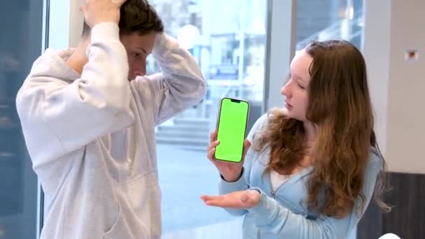 překvapený rozhořčení chlapec drží hlavu při pohledu na telefon se zelenou obrazovkou dívka říká ujišťování mávání hlavou chlapec souhlasí palce nahoru při pohledu do rámu teenageři proti řešení problému okna na telefonu - Záběry, video