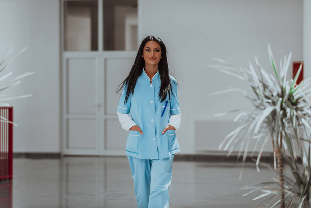 Pielęgniarka w niebieskim mundurze stojąca na korytarzu nowoczesnego szpitala.  - Zdjęcie, obraz