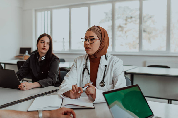 V moderní zasedací místnosti se muslimská lékařka v hidžábu zapojuje do diskuze se svými kolegy, která dokládá rozmanitost, inkluzivitu a společné řešení problémů - Fotografie, Obrázek
