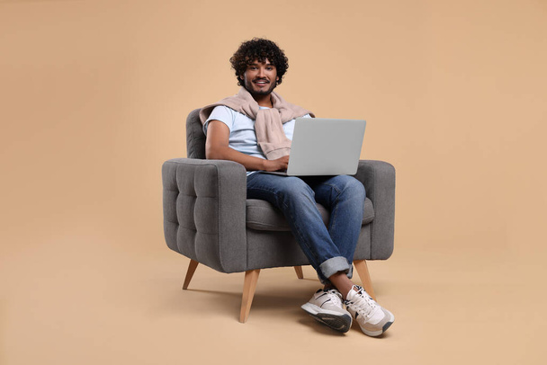 Smiling man with laptop sitting in armchair on beige background - Foto, Imagem