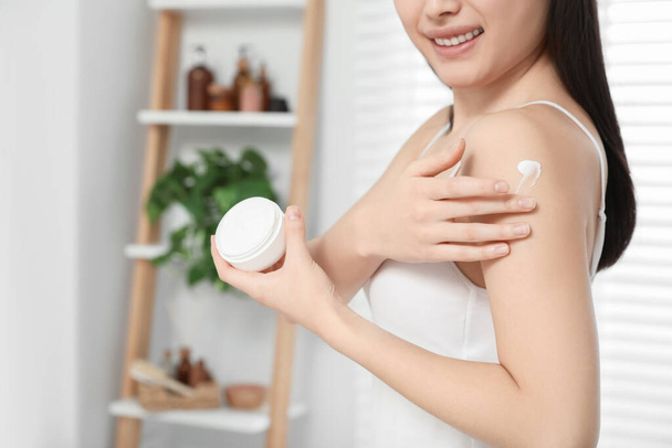 Young woman applying body cream on shoulder in room, closeup. Space for text - Fotoğraf, Görsel