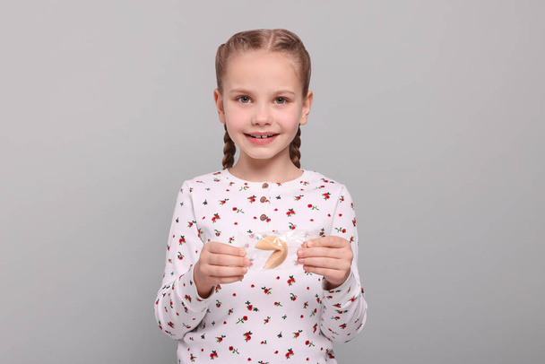 Cute girl holding tasty fortune cookie with prediction on light grey background - Fotografie, Obrázek