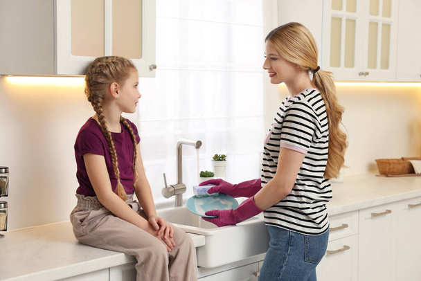 Mother washing plate while speaking with daughter in kitchen - Photo, Image
