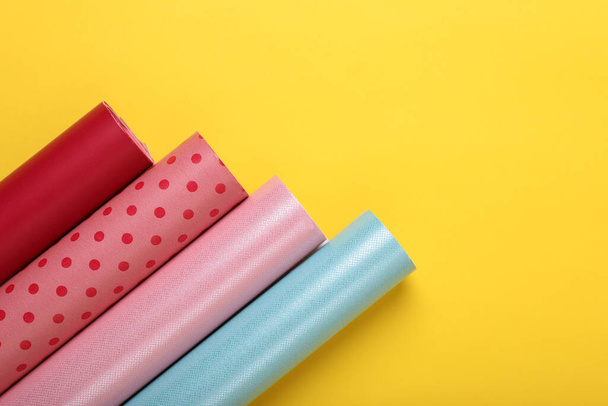 Rolls of colorful wrapping papers on yellow background, flat lay. Space for text - Foto, Imagem