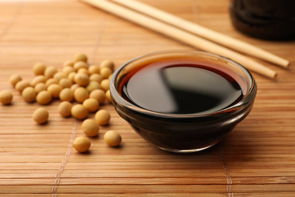 Soy sauce in bowl and soybeans on bamboo mat, closeup - Foto, Imagen