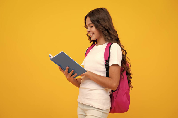 Schulmädchen mit Schulranzen-Rucksack halten Buch auf gelbem isolierten Studiohintergrund. Schul- und Bildungskonzept für Kinder - Foto, Bild