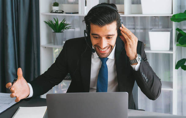 Male call center operator or telesales representative siting at his office desk wearing headset and in conversation with client providing customer service support or making persuasive sale. fervent - Foto, imagen