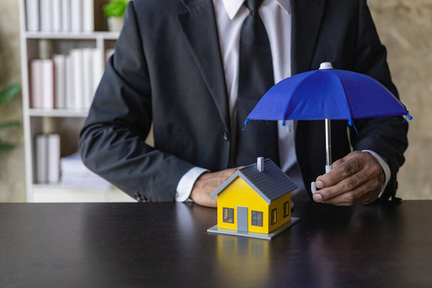 verzekeringsbedrijf De agent verspreidt de paraplu over het huis. Het concept van preventie van gezondheidsongevallen en natuurrampen, een close-up-beeld. - Foto, afbeelding