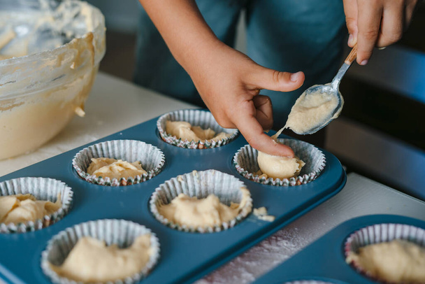 A childs hand pouring batter into cups during a home baking workshop, making cupcakes. Food preparation. Fun family. - Foto, Bild