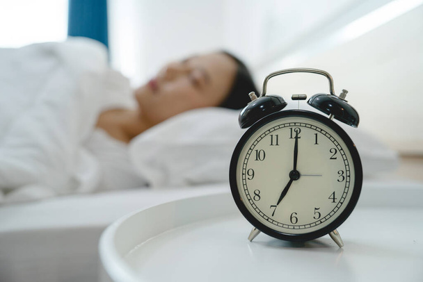 Asian woman resting in bed with alarm clock - Фото, зображення