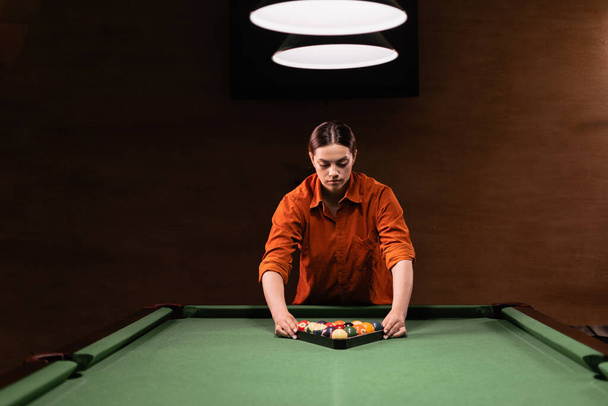 Sports game of billiards on a green cloth. Caucasian woman collect multi colored billiard balls in the form of a triangle with numbers shoot. Sports games, outdoor activities. Copy space - Foto, immagini