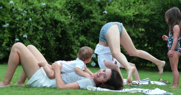 外の芝生で子供と赤ちゃんとヨガの練習をしている母親 - 写真・画像