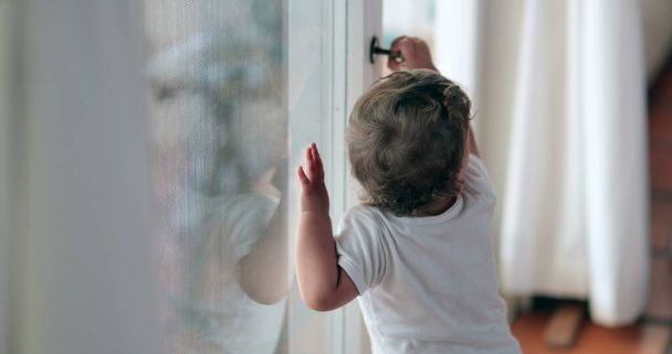 Baby toddler wanting to go outside holding window knob - Foto, imagen