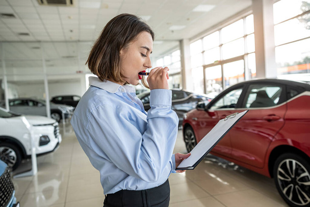  female salesperson alone at car dealership holding tablet and waiting customer. sale concept - Foto, imagen
