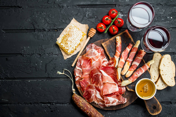 Spanish ham with red wine and breadsticks. On black rustic background. - Photo, Image