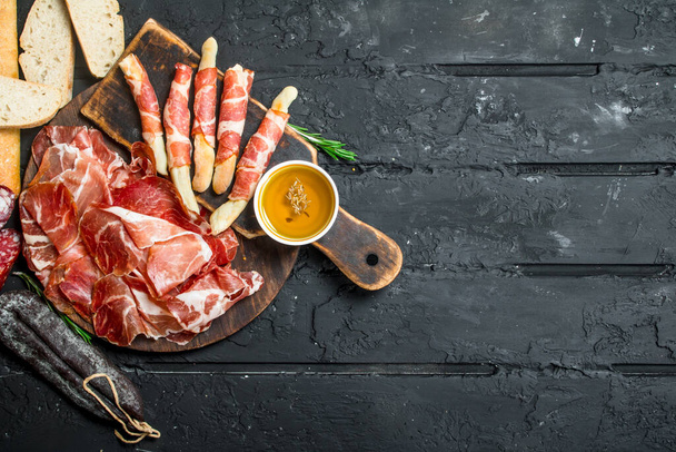 Traditional Spanish ham with ciabatta and breadsticks. On black rustic background. - Foto, Imagen