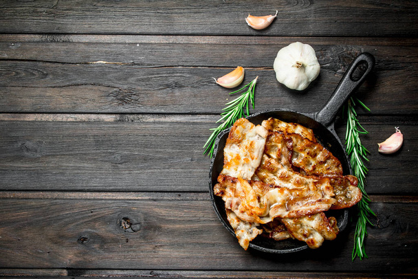 Fried bacon in a pan with spices and rosemary. On a wooden background. - Photo, image