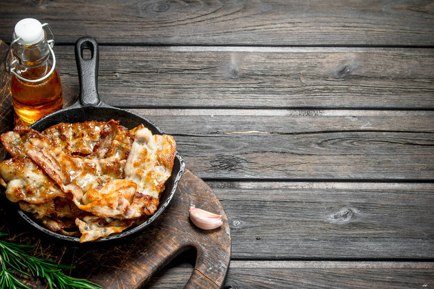 Fried bacon in a pan with spices and rosemary. On a wooden background. - Photo, Image