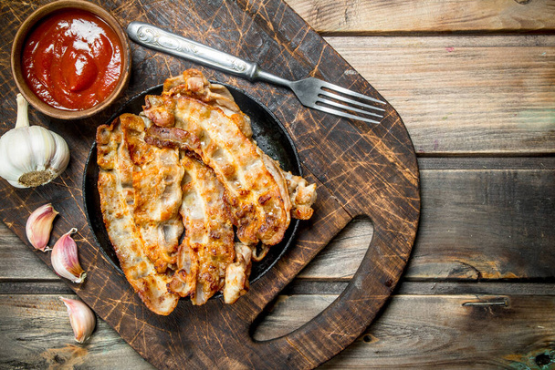 Fried bacon with tomato sauce. On a wooden background. - Фото, изображение
